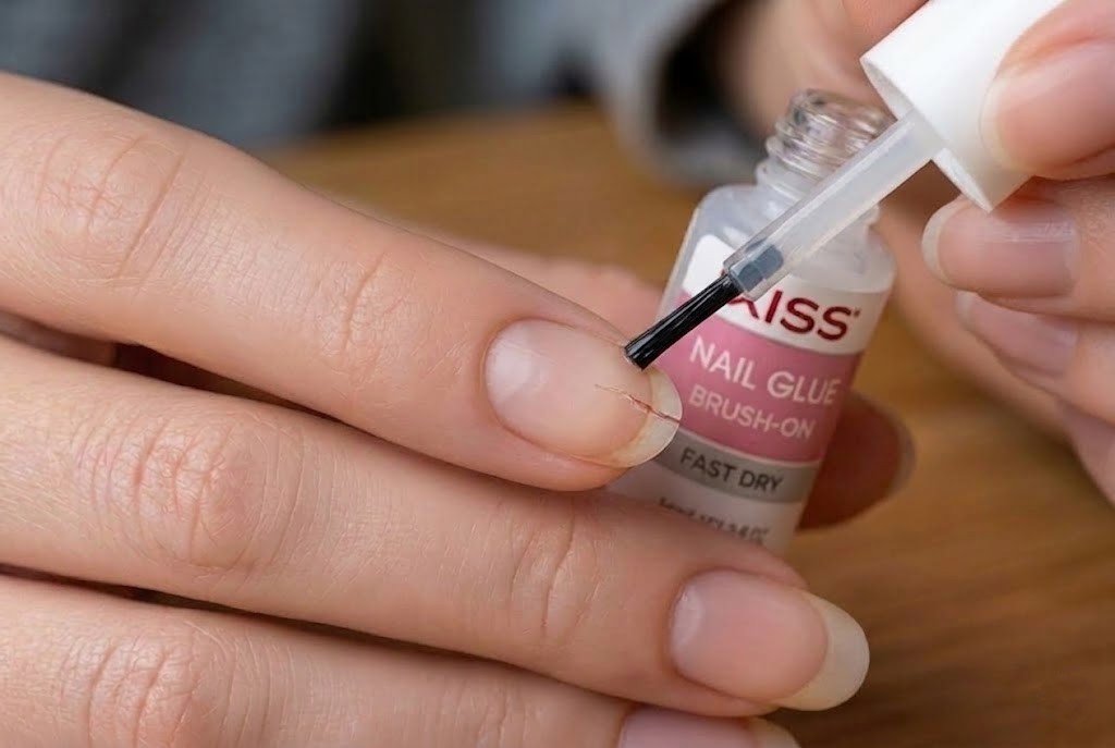 brush-on nail glue being applied to a cracked fingernail at home using a KISS nail glue bottle
