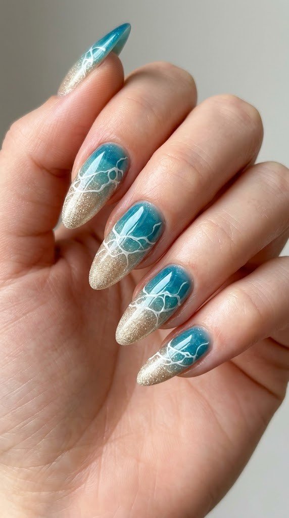 Almond nails with sandy gold glitter tips fading to translucent teal beach gradient