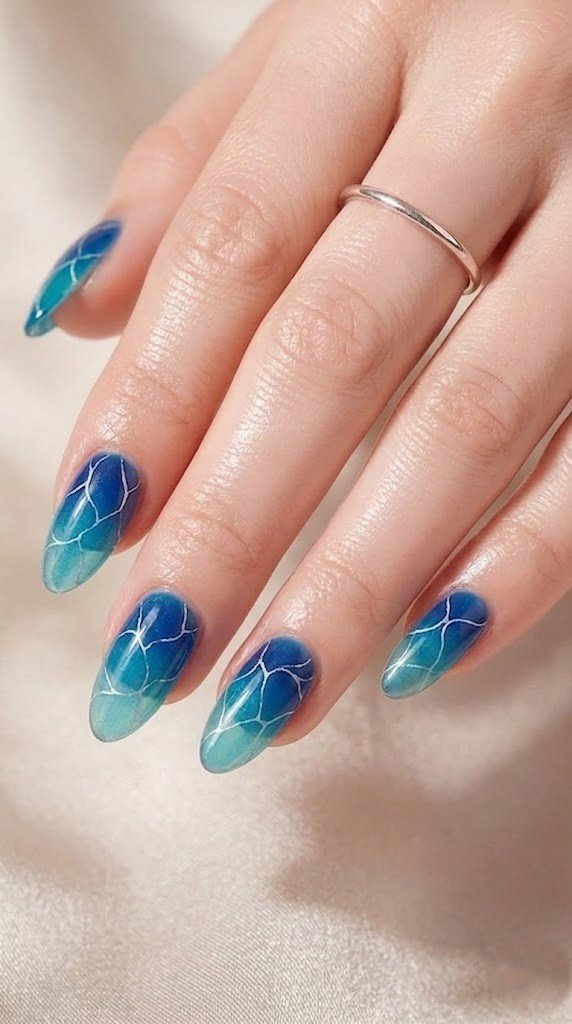 Almond nails with ocean ripple gradient from deep royal blue to seafoam green with white veining