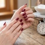 How long does nail polish take to dry shown with dark red almond nails, stopwatch, and Seche Vite top coat bottle