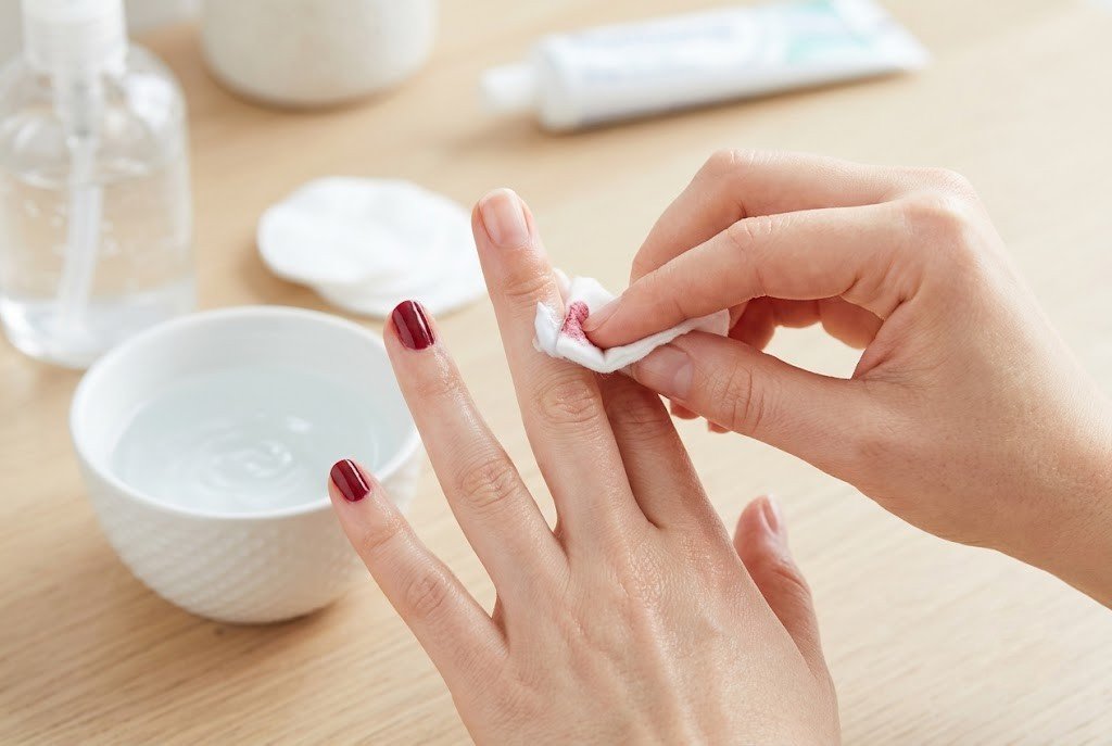 Woman removing dark red nail polish with a cotton pad using toothpaste method at home