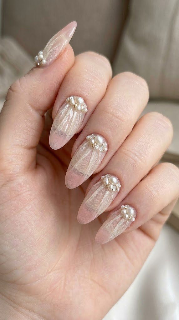 Nude pink almond nails with white tulle texture and 3D pearl rhinestone gold bead cluster at cuticle